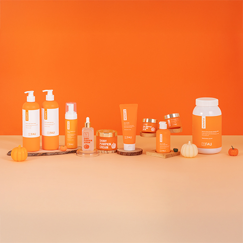 FAU Pumpkin skincare line products displayed on an orange background, featuring lotion, cream, ampoule, and cleanser bottles.