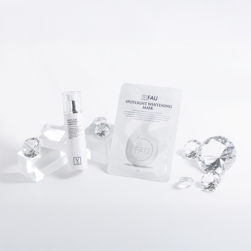 FAU Spotlight Whitening skincare products, including a brightening ampoule and mask sheet, displayed with crystal decorations on a white background.