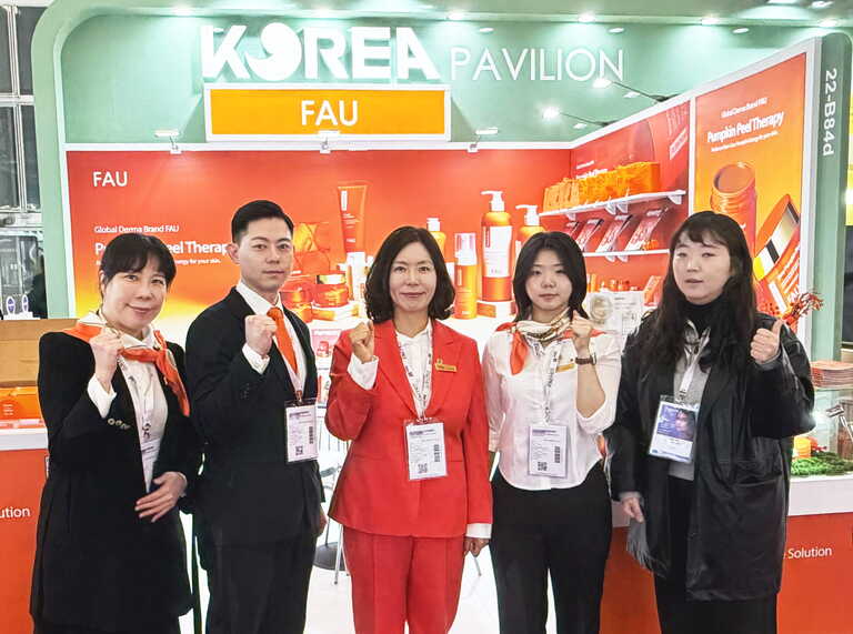 FAU representative team in orange uniforms posing at Cosmoprof Worldwide Bologna 2026 Korea Pavilion booth.